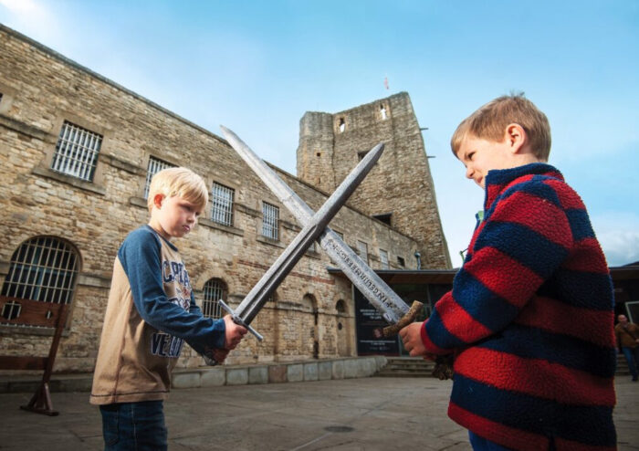 Two children cross swords in front of a castle