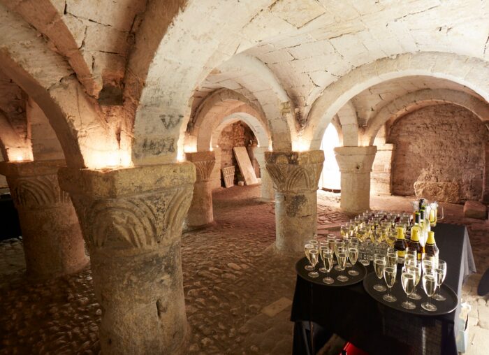A underground crypt with a table in the foreground with champagne bottles and glasses on it
